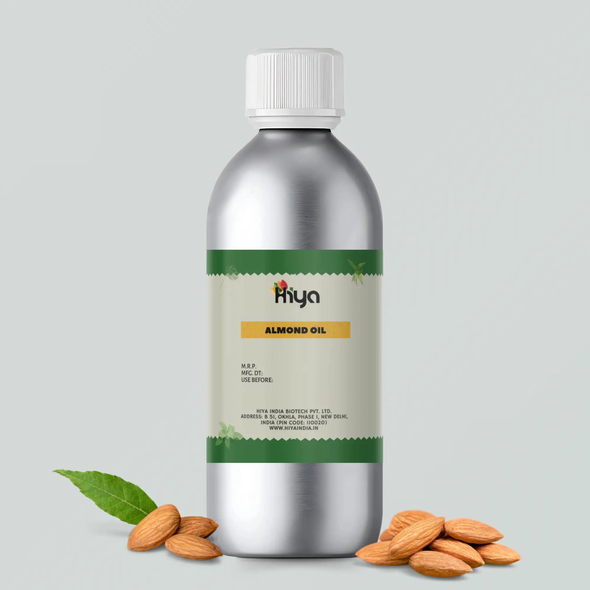 Hiya India Almond Oil metallic bottle with a white cap and green-beige label, featuring product details such as MRP, manufacturing and expiration dates, and the manufacturer's address: Hiya India Biotech Pvt. Ltd., located in New Delhi, India. The bottle is surrounded by whole almonds and a green leaf, highlighting the natural essence of the oil.
