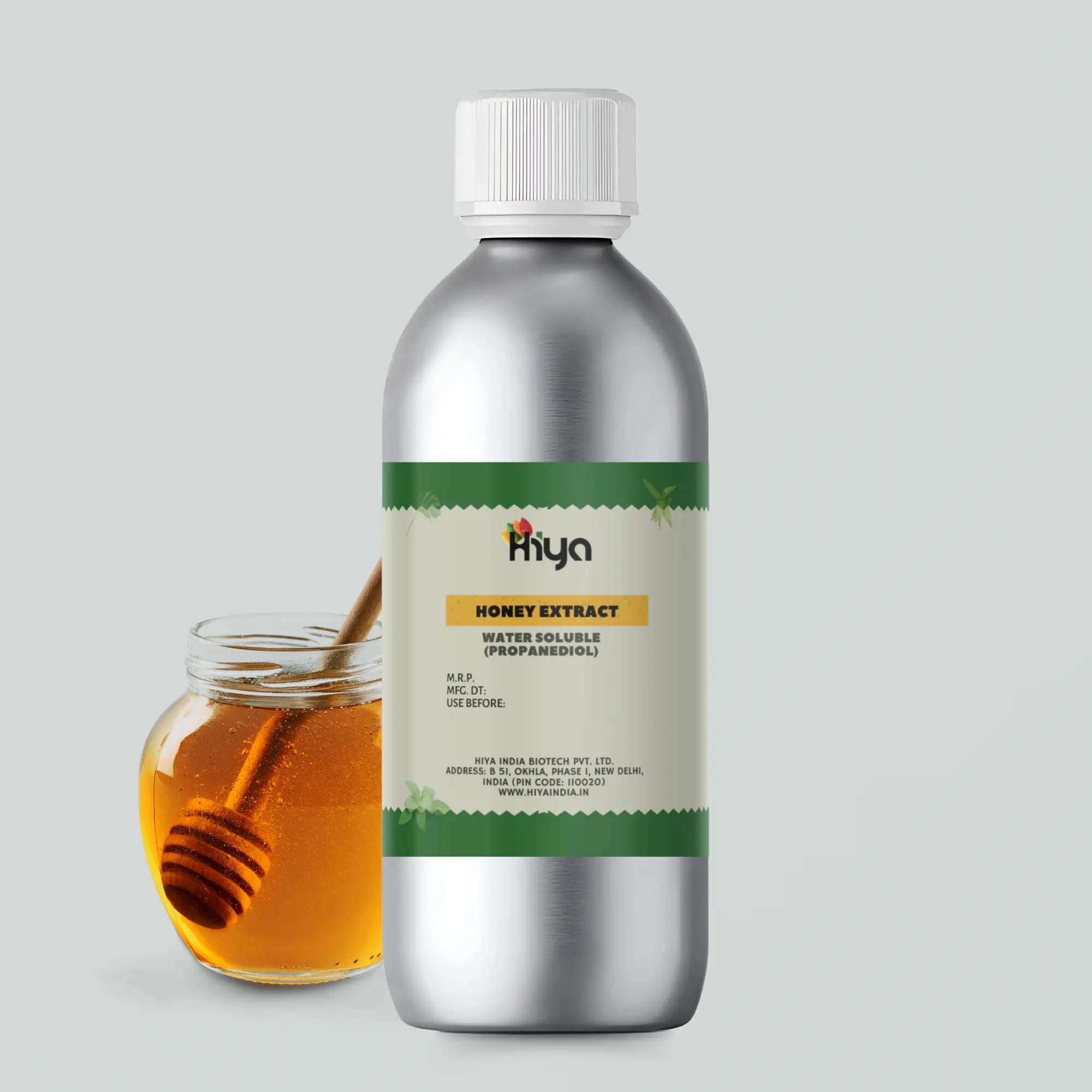 A silver bottle labeled "Hiya Honey Extract Water Soluble (Propanediol)" stands upright. The label includes the product name, manufacturing details, and expiration information. To the side, a glass jar filled with golden honey sits with a wooden honey dipper resting inside, showcasing the honey’s thick texture.