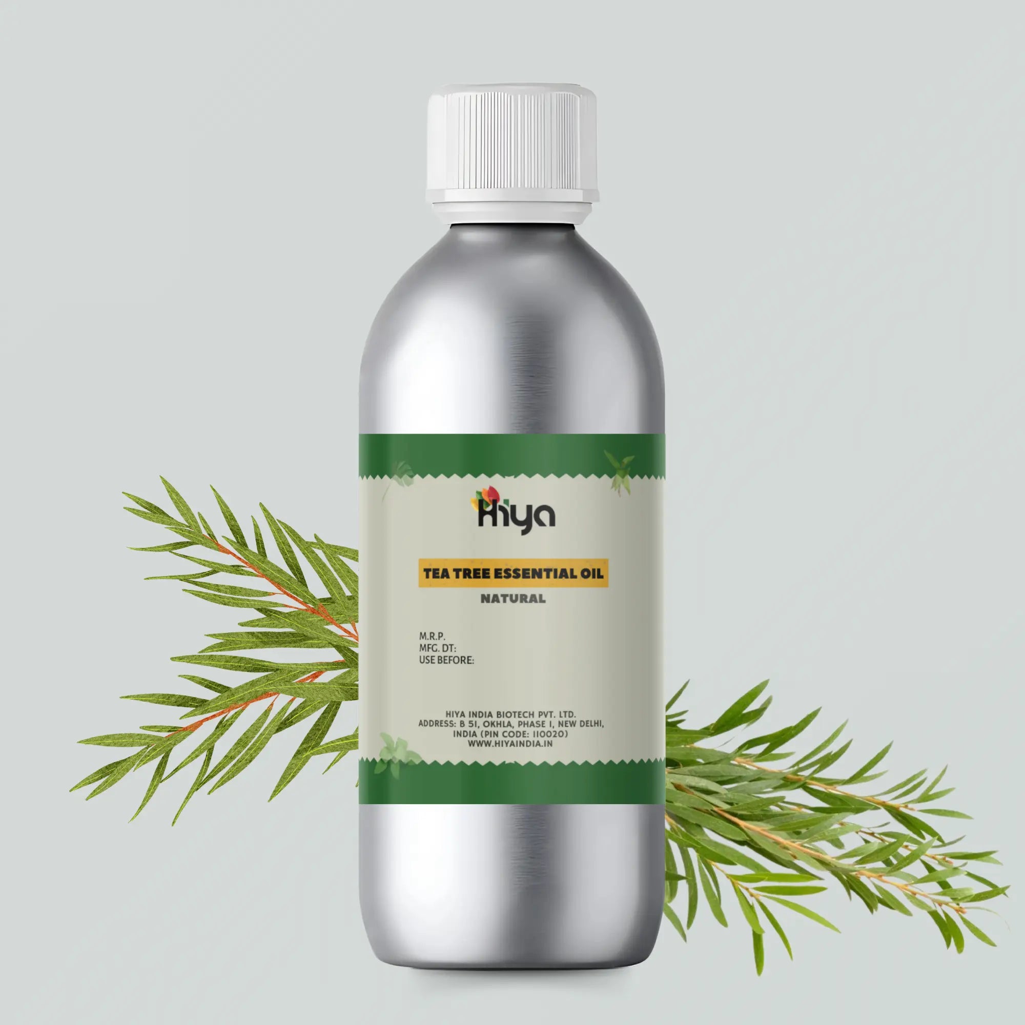 Hiya Tea Tree Essential Oil bottle with a metallic finish and white cap, featuring a green label. The label reads "Natural Tea Tree Essential Oil" by Hiya India Biotech Pvt. Ltd., New Delhi, India. Sprigs of fresh tea tree leaves surround the bottle, emphasizing its natural ingredients and benefits for aromatherapy and skin care.